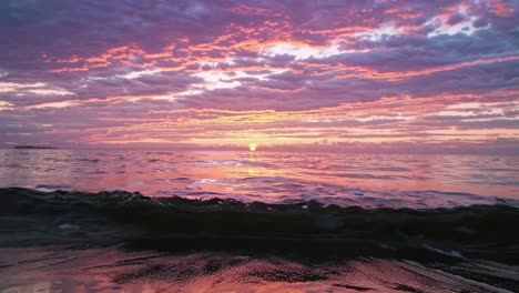 low-angle video capture of a vibrant sunset over the ocean, with dramatic clouds and reflections