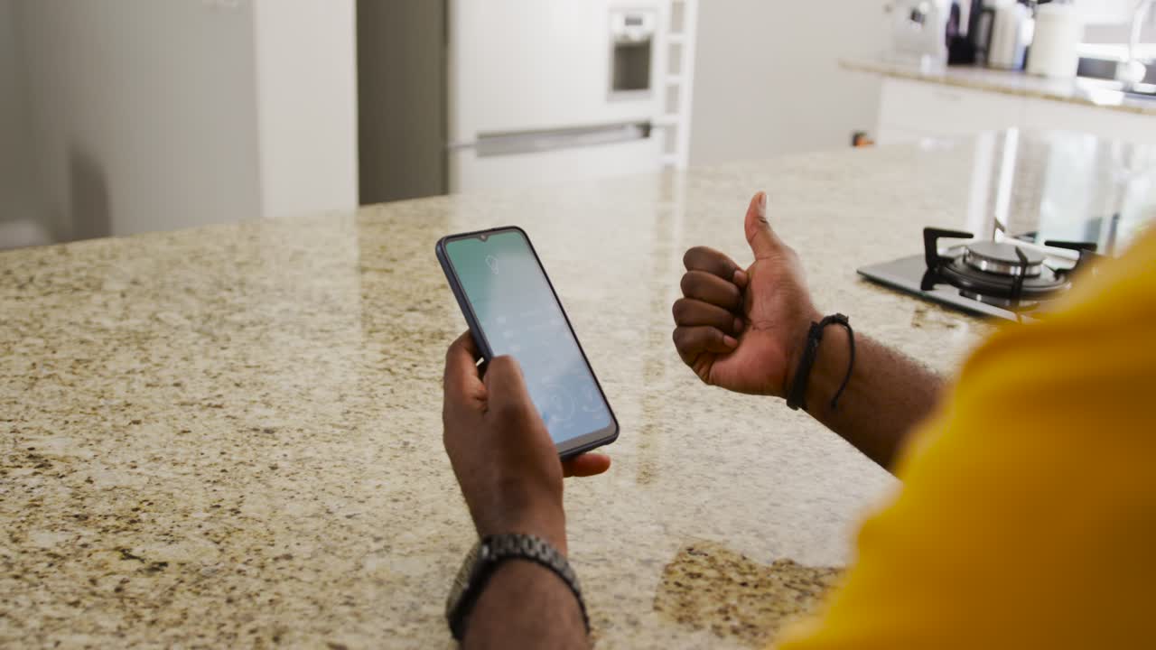 African man with phone screen at kitchen scrolling thumbs-up pointing open-palm tapping, copy space