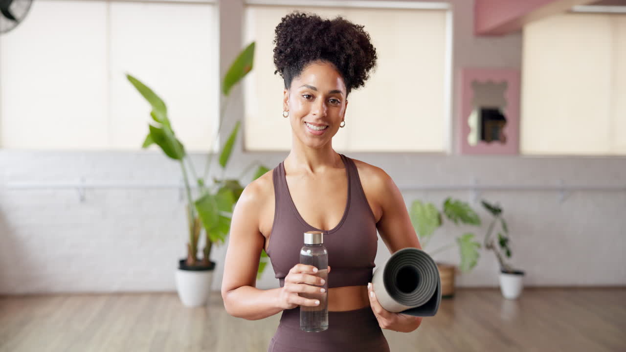 Donna che tiene in mano un tappetino da yoga e una bottiglia d'acqua in uno studio fitness