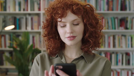 Retrato-De-Una-Encantadora-Joven-Bibliotecaria-Parada-En-La-Biblioteca-Usando-Un-Teléfono-Inteligente-Estudiante-Atractiva-Sonriendo-Cerca-De-Compras-En-Línea