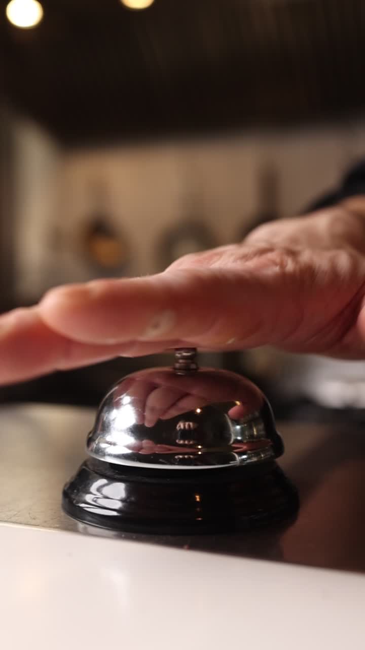 Una mano suona un campanello di servizio in metallo sul bancone