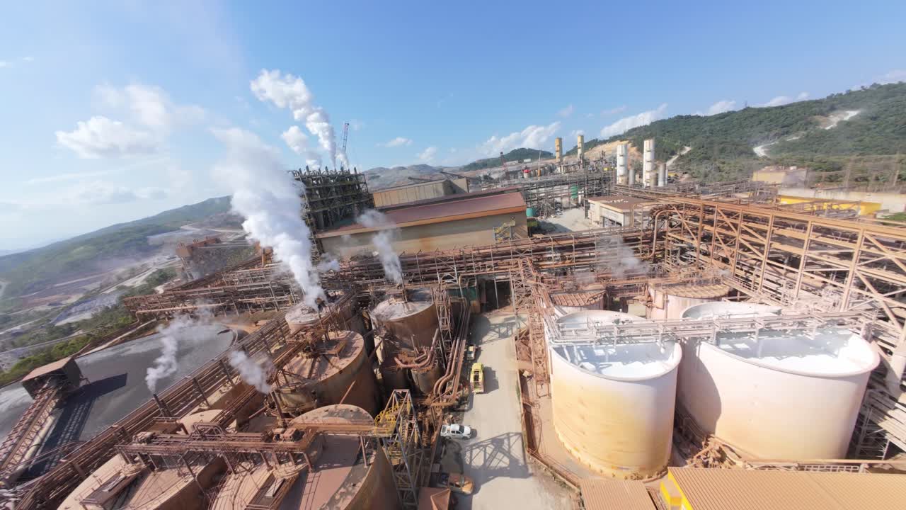 Steam or emissions from the mining operation rising into sky. Aerial fpv flight over mining complex factory in Cotui, Dominican Republic.