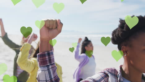 múltiples corazones verdes flotando contra un grupo de personas diversas que protestan en la playa