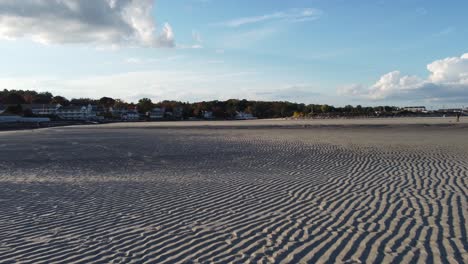 Drohnenflug-über-Sandstrand-Mit-Dünenmuster-Und-Wasserhimmelspiegelung