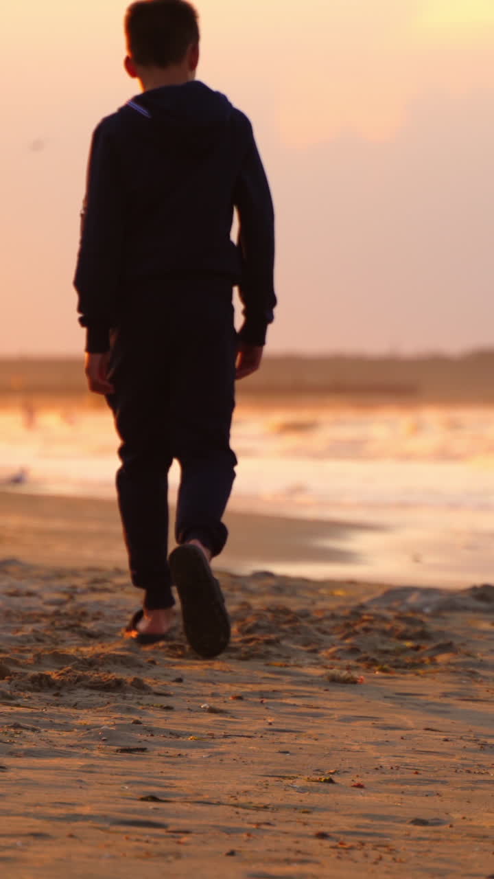 Boy walking at beach on sunset. Boy walking alone on the beach during sunset at seaside