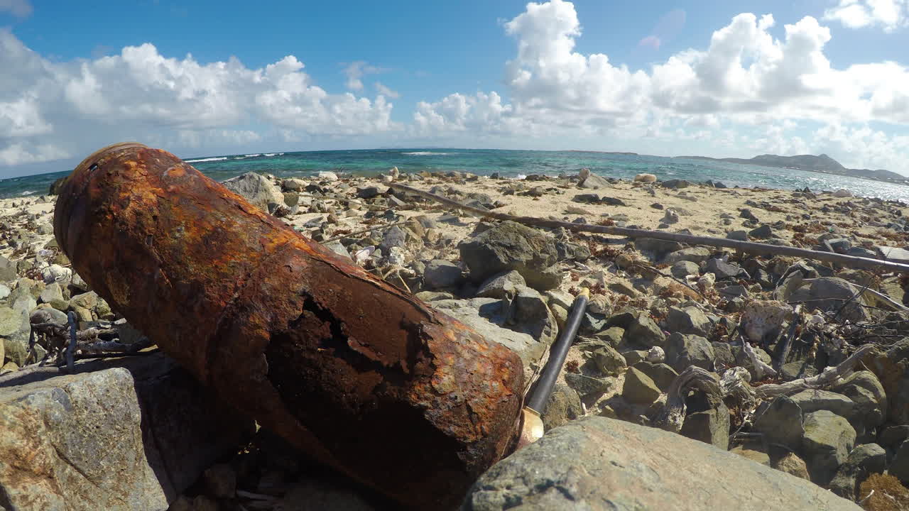 Ilha Pinel, Saint Martin, mostrando praia rochosa, lixo e o oceano ao fundo. Perfeito para projetos de reciclagem, impacto humano do turismo e natureza.