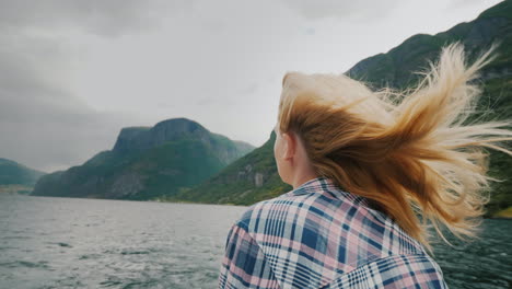a young woman with flowing hair is standing on the bow of the ship looking forward the wind blows in