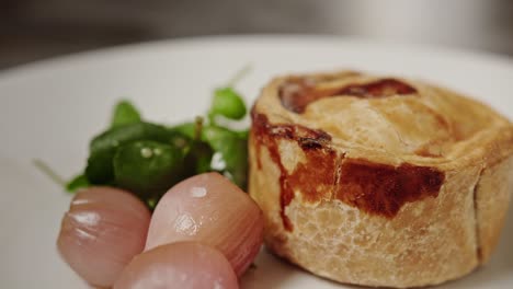 a pork pie is served on a plate with two picked onions