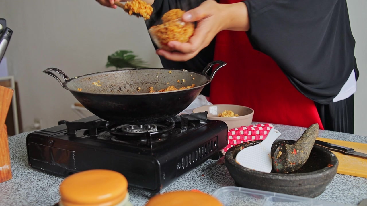 Koki mengemas nasi goreng yang baru dimasak ke dalam cetakan mangkuk dari wajan di atas kompor dapur.