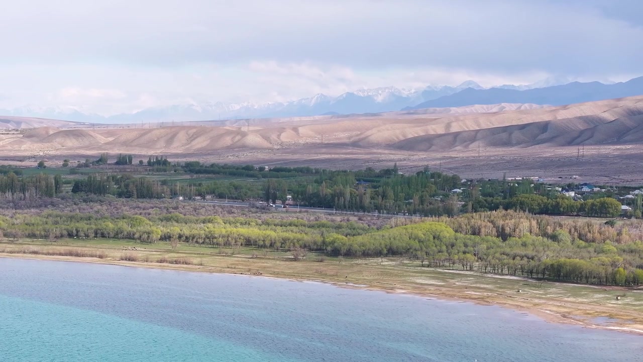 Kırgızistan'daki Issık Göl'ün güney kıyısı, dağ silsilesi ve küçük bir yerleşim yeri ile.