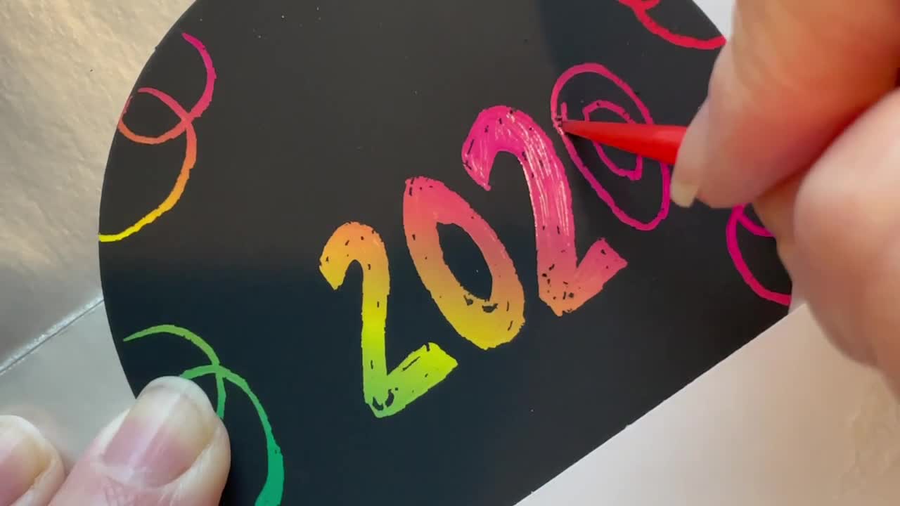 Hånd som etser 2020 i farger på en svart bakgrunn.