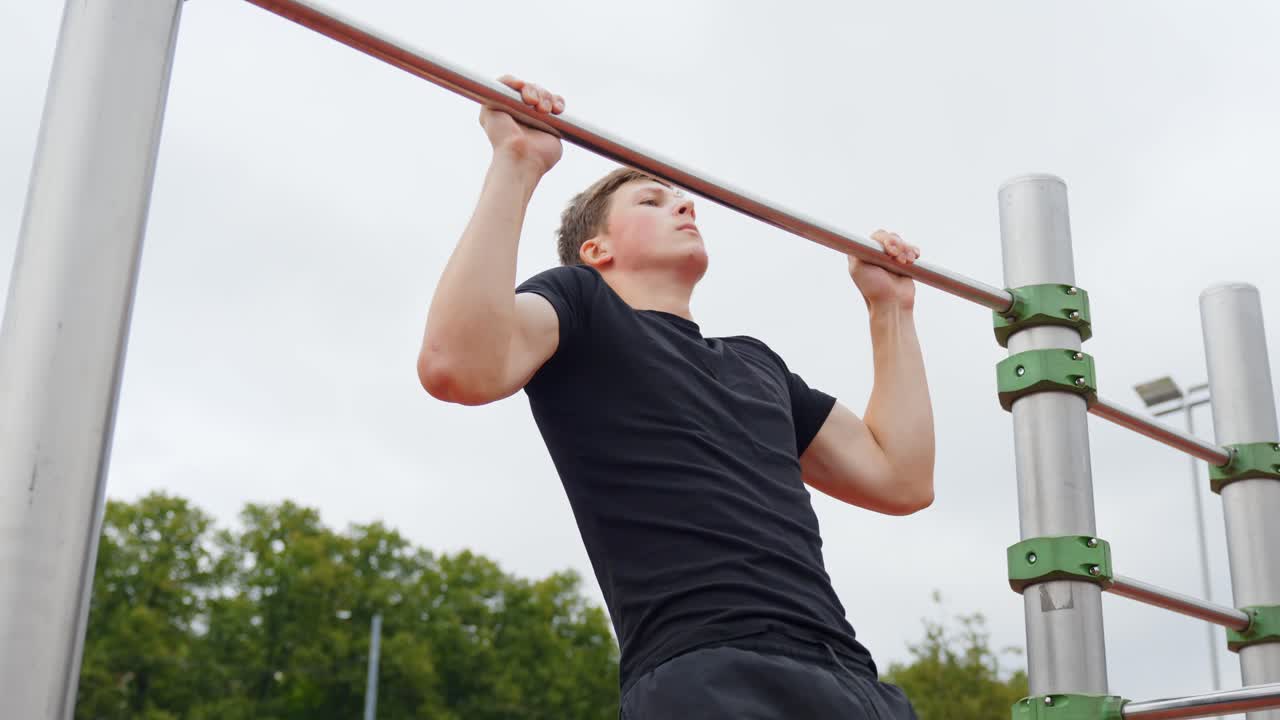 Young caucasian man doing intense pull up exercise on a horizontal bar at an outdoor fitness park, demonstrating dedication to calisthenics, fitness, and strength training, slow motion, static camera