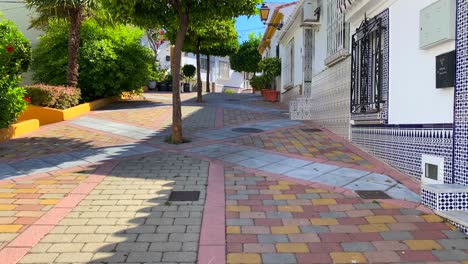 Orange-trees-and-palm-trees-in-a-typical-little-Spanish-street-with-houses-in-Marbella-old-town,-sunny-day-and-blue-sky-in-Spain,-4K-tilting-up