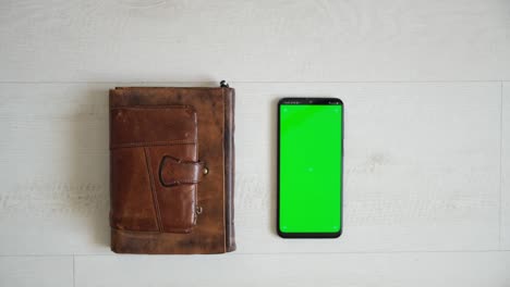 phone with green screen on the table with notebook and purse view from top, smartphone chromakey screen copy space
