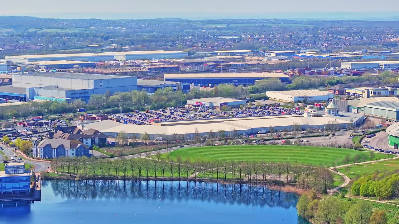 High-angle aerial view of the Doncaster Lakeside Shopping area in South Yorkshire, England, with retail buildings, packed parking lots, landscaped green spaces, and lake edge clearly visible