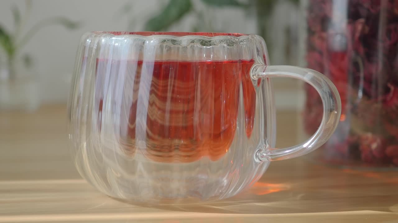 Tè caldo all'ibisco in una tazza di vetro trasparente su un tavolo di legno