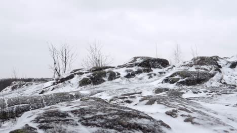 rocky-hills-lightly-covered-in-snow,-light-snowfall,-pan-left