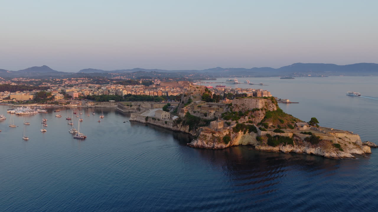 Sunrise light hitting the Old Fortress of Corfu with calm sea surrounding the site, panoramic aerial tracking left establish
