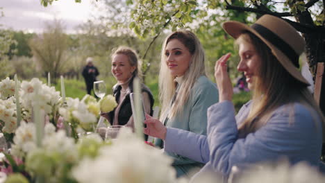 young women are dining in garden in spring day friendly party in weekend lunch in blooming orchard