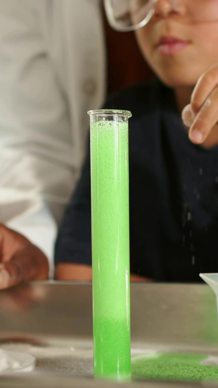 Vertical video: Adding powder adult in lab coat making green foam rising in tube in class