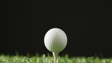 Close-up-of-golf-tee-and-ball-on-grass-and-black-background,-copy-space,-slow-motion