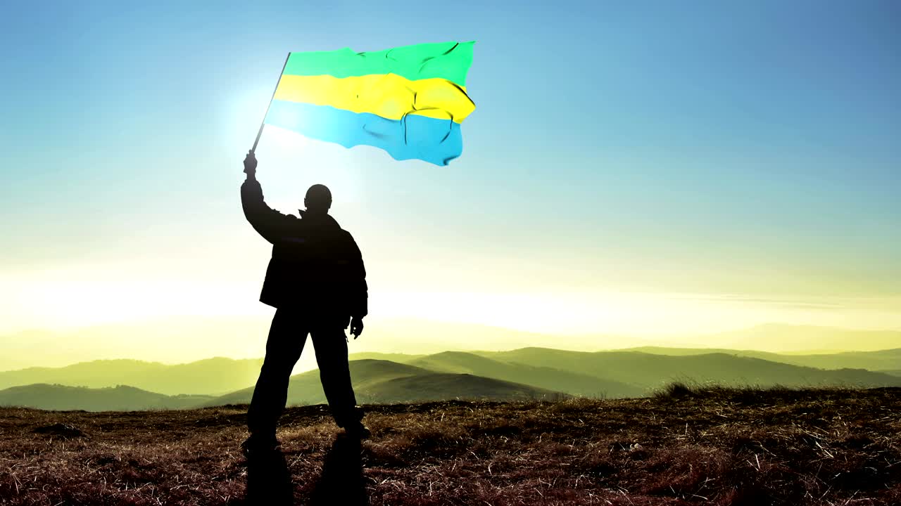 Uomo vincitore in silhouette che sventola la bandiera del Gabon in cima alla vetta della montagna. Sfondo Cinemagraph in LOOP