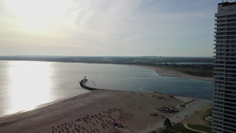 Kletterflug-über-Einen-Strand-Mit-Leuchtturm-Auf-Der-Landzunge-Im-Hintergrund