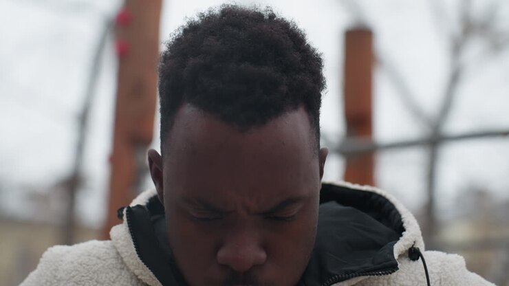 Close-up of determined sports enthusiast engaging in outdoor fitness training during winter, man wears warm fleece jacket with hood, standing near wooden workout structure with blurred background