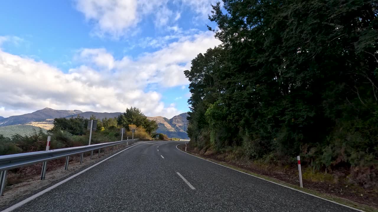 Point-of-view drive on winding rural road, lush forest, lake, mountains, daylight, smooth camera motion