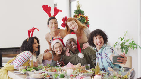 happy group of diverse friends sitting at table and eating dinner together, taking selfie