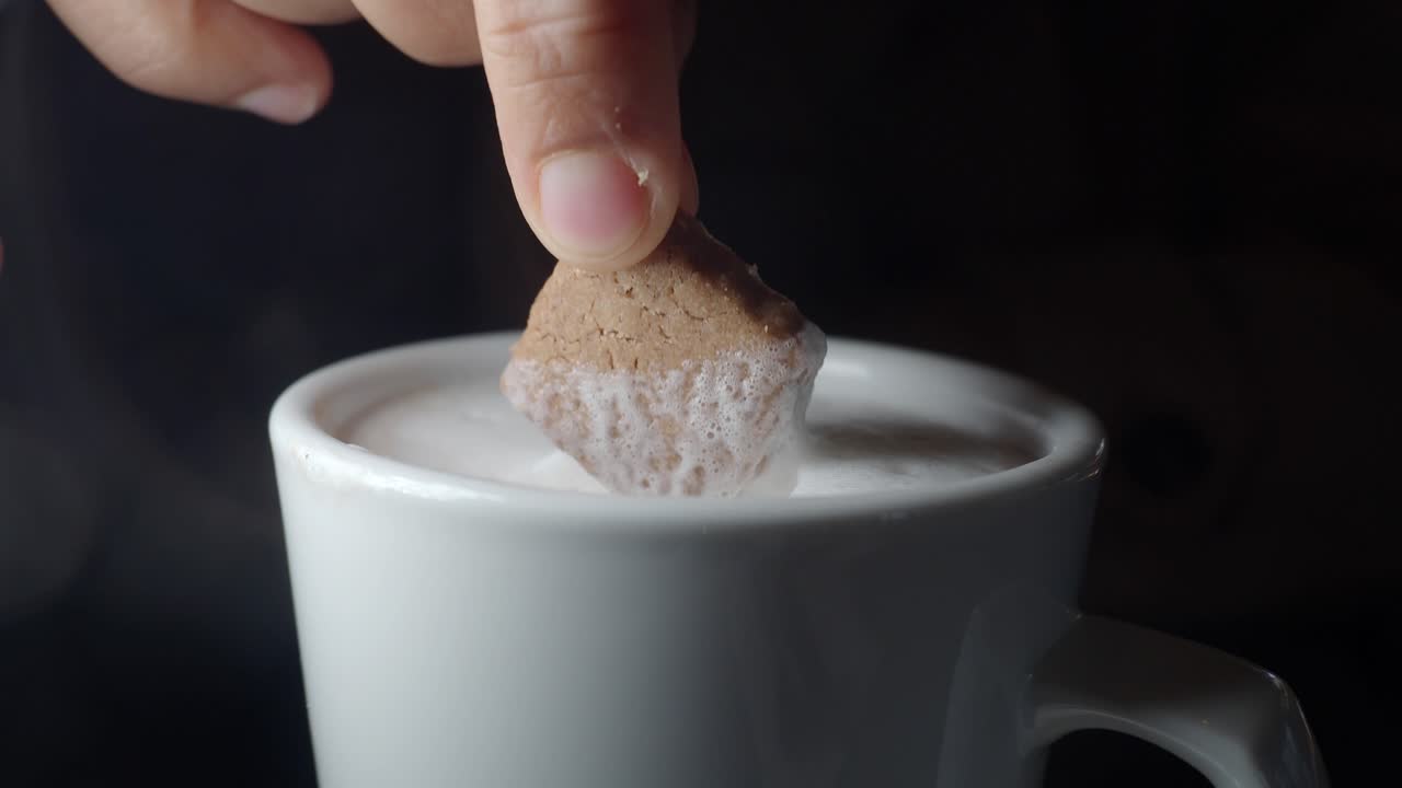 Primo piano di mano che intinge un biscotto in una bevanda calda e spumosa