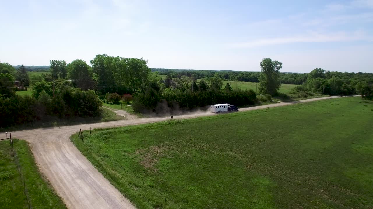 Grande rimorchio per cavalli in vista aerea trainato da un pickup nero che percorre rumorosamente una strada sterrata rurale in lontananza, Kansas, Missouri. Concetto: avventura, la strada meno battuta, rurale