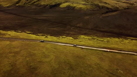 Aerial-view-over-two-four-wheel-drive-cars-traveling-on-a-dirt-road-through-icelandic-highlands