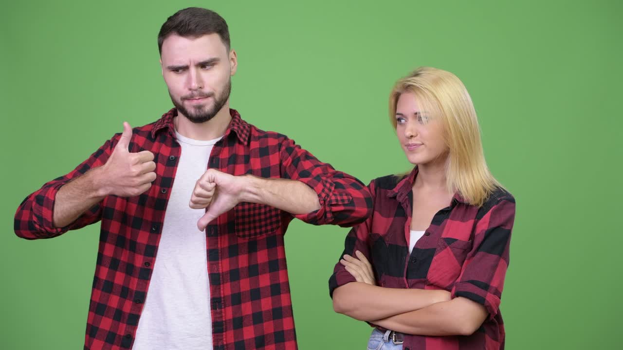 Young man being indecisive with young woman waiting with arms crossed