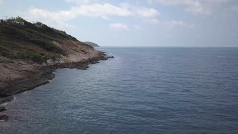 Antena:-Vista-Del-Paisaje-De-Una-Playa-Rocosa-Una-Pequeña-Colina-En-El-Lado-Izquierdo,-Con-Olas-Provenientes-Del-Océano