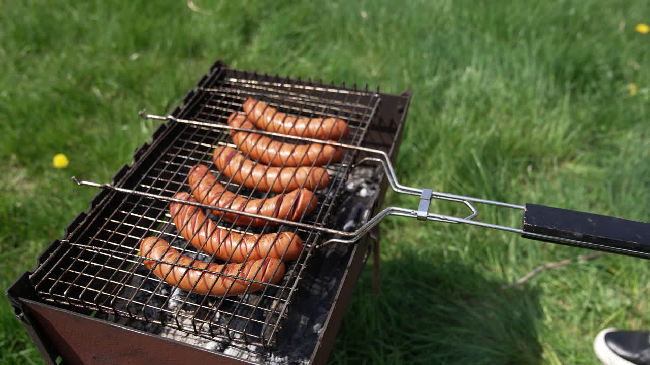 Barbecue grill. Cooking sausages for picnic. Hot dog sausages being cooked and turned over on an outdoor grill. Making a picnic.