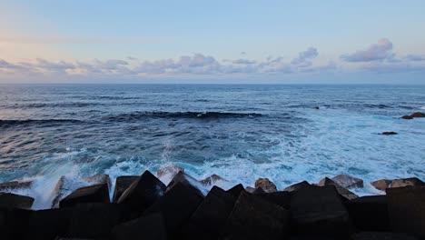 ocean waves crashing into breakwater from angular rocks and splashing in the evening