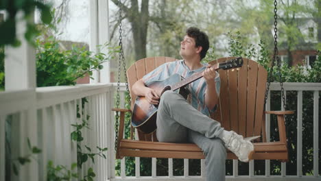 man playing guitar on a porch swing