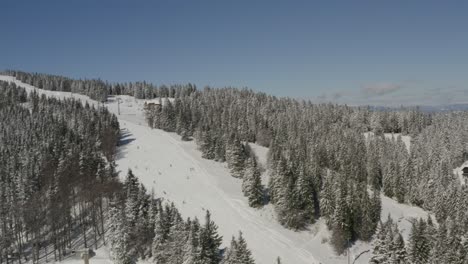 kope slovenia ski resort with ribnica one track with skiers descending the slopes, aerial pan right shot