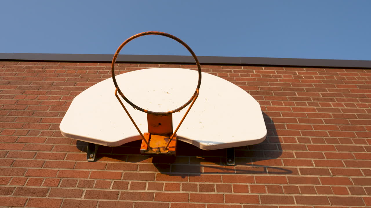 Looking up at a basketball hoop on the brick wall of a schoolyard on a sunny morning