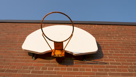 looking up at a basketball hoop on the brick wall of a schoolyard on a sunny morning