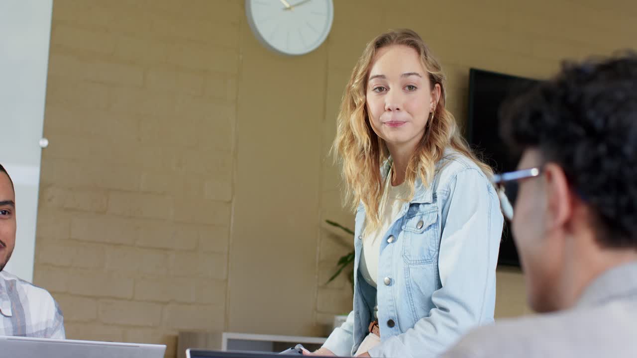 Mangfoldige kollegaer som tar notater ved bordet mens en kvinne i denim flytter blikket og presenterer viktige beregninger