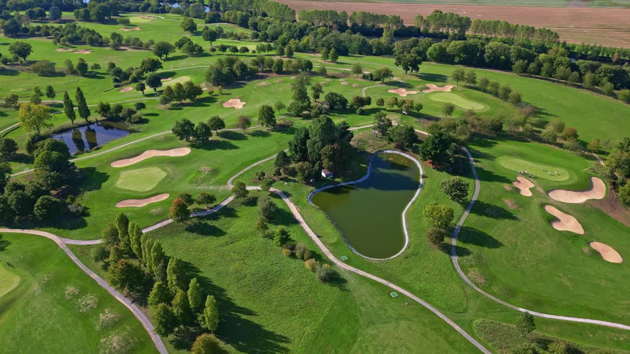 Drone flying backward in top-down view over a golf course with sand bunkers, ponds, trees, and connecting paths