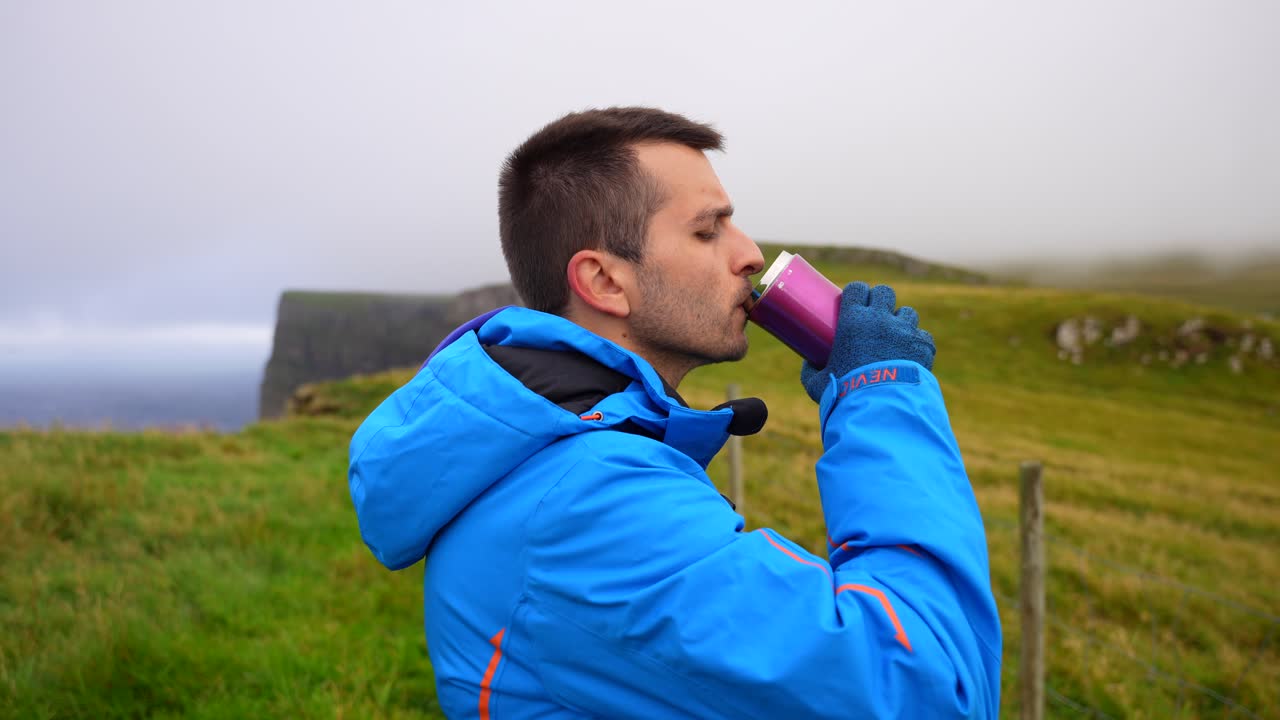 el hombre abre el frasco para beber, se pone la sudadera y continúa la caminata en mykines, islas feroe