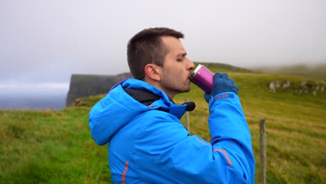 El-Hombre-Abre-El-Matraz-Para-Beber,-Se-Pone-Una-Sudadera-Con-Capucha-Y-Continúa-Caminando-En-Mykines,-Islas-Feroe.