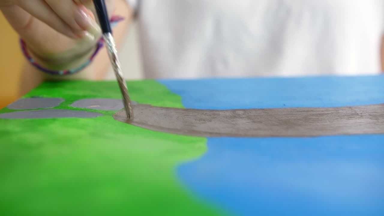primer plano de cámara lenta de niña pintando trazo gris con pincel, colores azul y verde