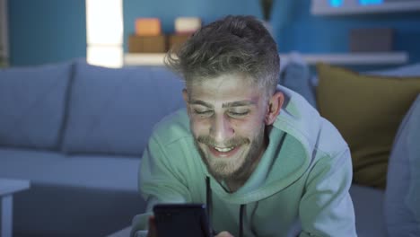 Charismatic-and-sympathetic-young-man-using-phone-at-home-in-a-happy-and-fun-mood.