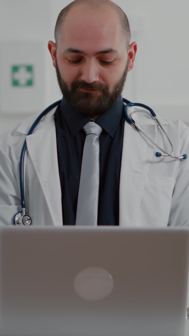 Vertical video: Front view of practitioner doctor typing illness expertise on computer
