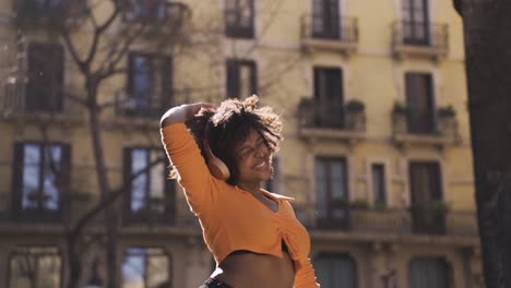 Cheerful-black-woman-dancing-in-headphones-on-street