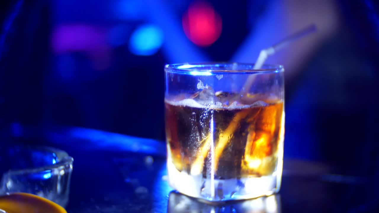 Primo piano di un cocktail alcolico in un bicchiere sul bancone del bar, in discoteca. Sfondo sfocato, 4k.